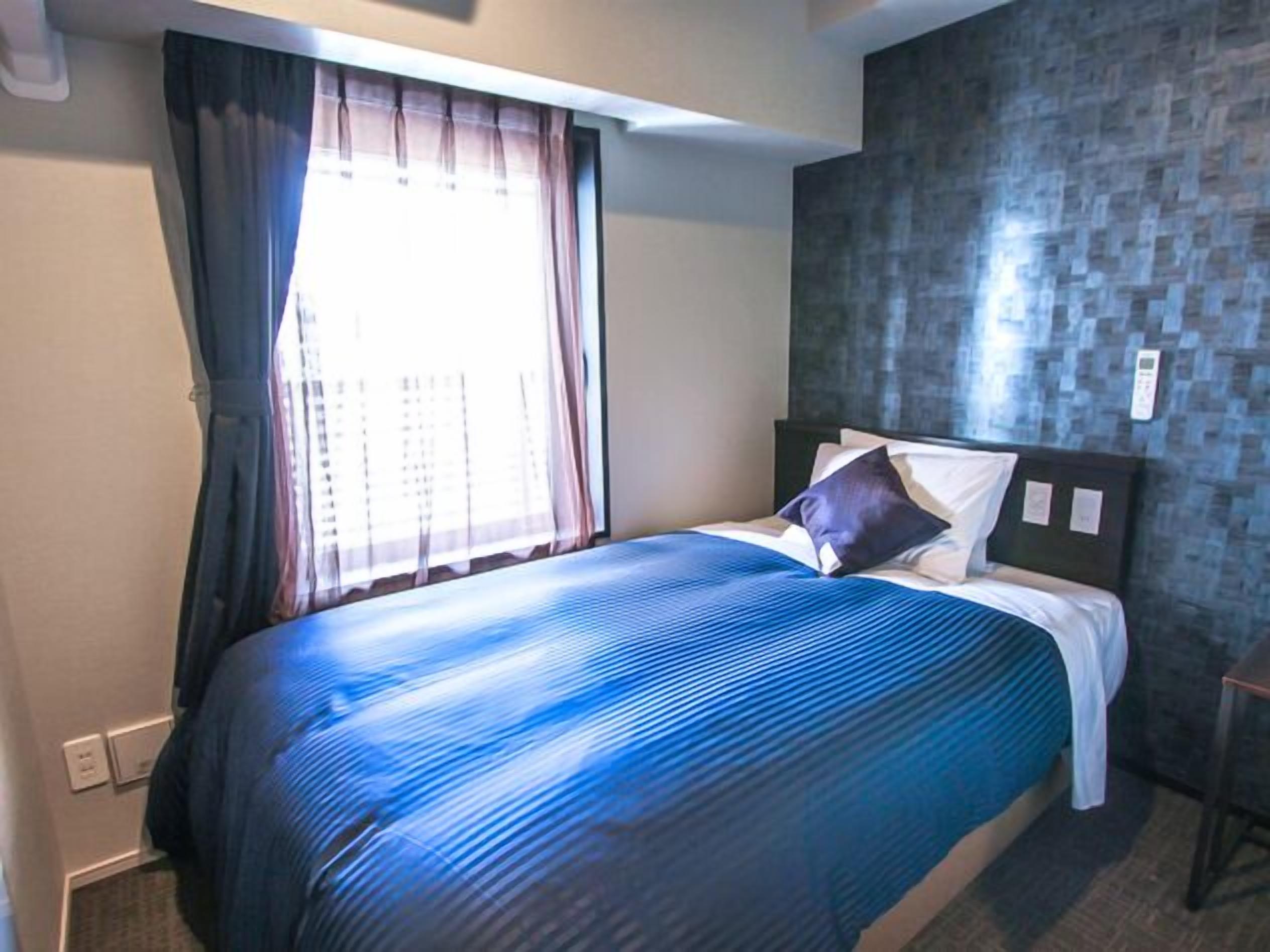 A hotel room with a bed, curtains, a wall with a textured pattern, and a small table.