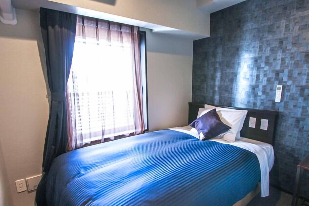 A hotel room with a bed, curtains, a wall with a textured pattern, and a small table.