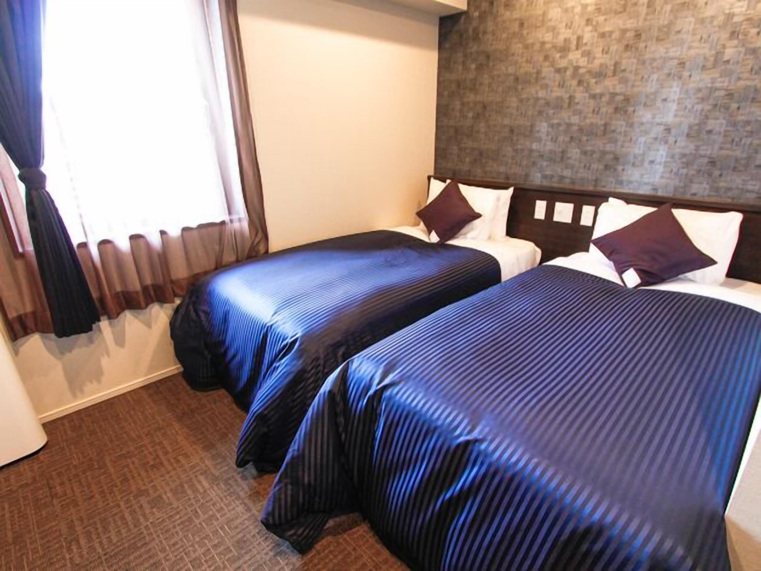 A hotel room with two beds, a wooden headboard, a brick-patterned wall, and a window with curtains.