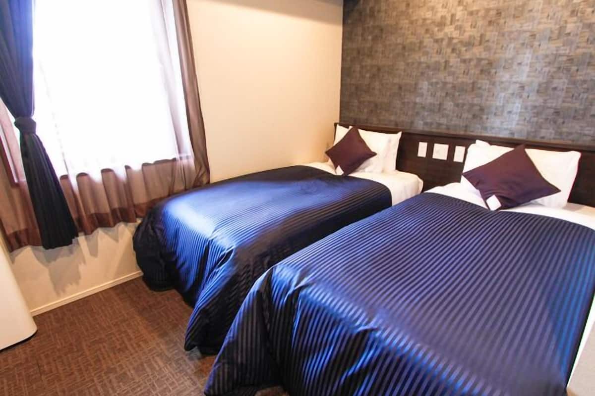 A hotel room with two beds, a wooden headboard, a brick-patterned wall, and a window with curtains.