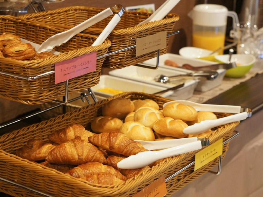 Ein Frühstücksbuffet mit Körben voller Croissants und anderen Backwaren, dazu eine Kaffeemaschine und ein Saftspender.
