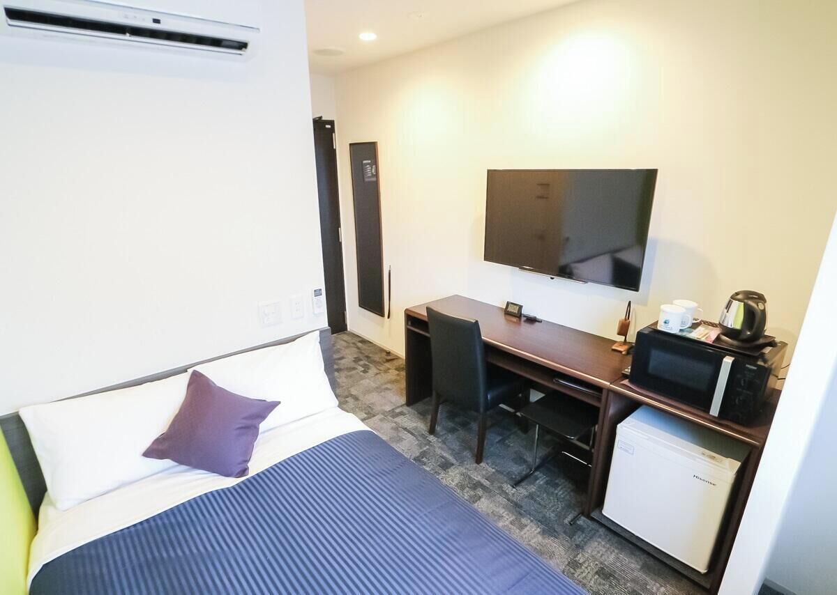 A hotel room with a bed, a desk, a television, a microwave, and a small refrigerator.