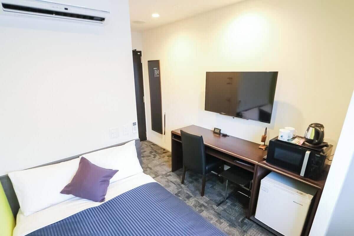 Ein Hotelzimmer mit einem Bett, einem Schreibtisch, einem Fernseher, einer Mikrowelle und einem kleinen Kühlschrank.