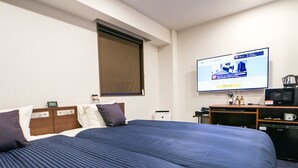 Ein Hotelzimmer mit einem großen Bett, einem an der Wand befestigten Fernseher, einer Kaffeemaschine und einem kleinen Kühlschrank.