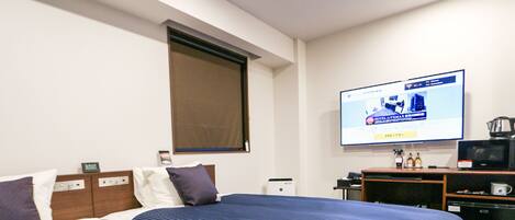 A hotel room with a large bed, a television mounted on the wall, a coffee maker, and a small refrigerator.