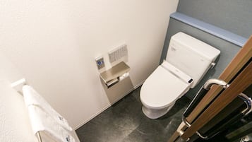 Ett litet, modernt badrum med en toalett, en handtork och en pappershandduksdispenser.