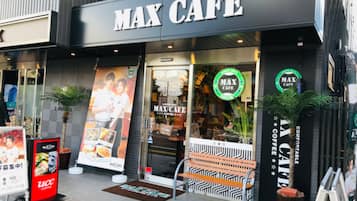 The exterior of a cafe with a prominent 'MAX CAFE' sign, a bench outside, and a potted plant to the right.