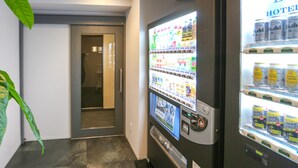 Ein Getränkeautomat mit verschiedenen Snacks und Getränken, ein mit Getränken gefüllter Kühlschrank und eine Tür zu einem Zimmer.