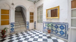 A hallway with a checkered floor, a staircase, and a tiled wall with a decorative border. - Apartamento Musa Catalina (Cádiz)