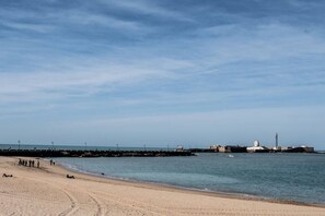 Une plage avec un ciel dégagé, un rivage sablonneux et une jetée qui s’avance dans l’eau.