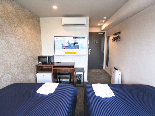 Una habitación de hotel con dos camas, un escritorio con computadora, televisión y aire acondicionado.