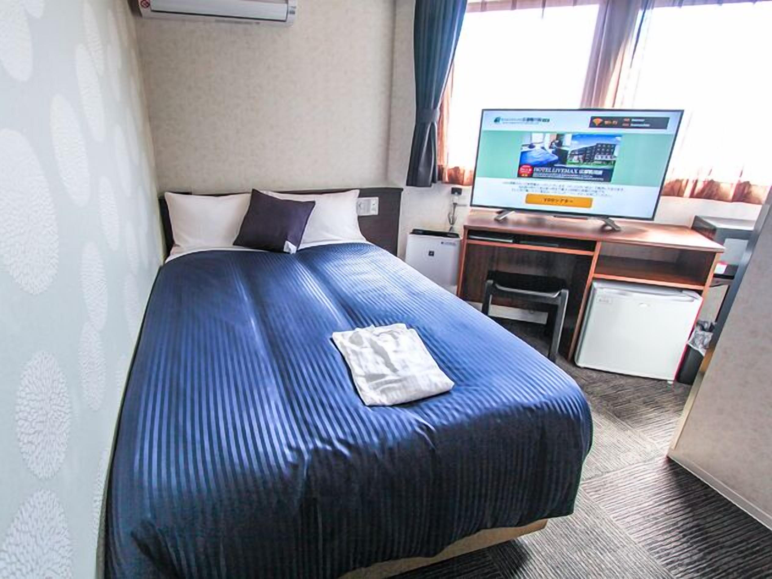 Una camera d'albergo con un letto, una scrivania, una televisione e un piccolo frigorifero.