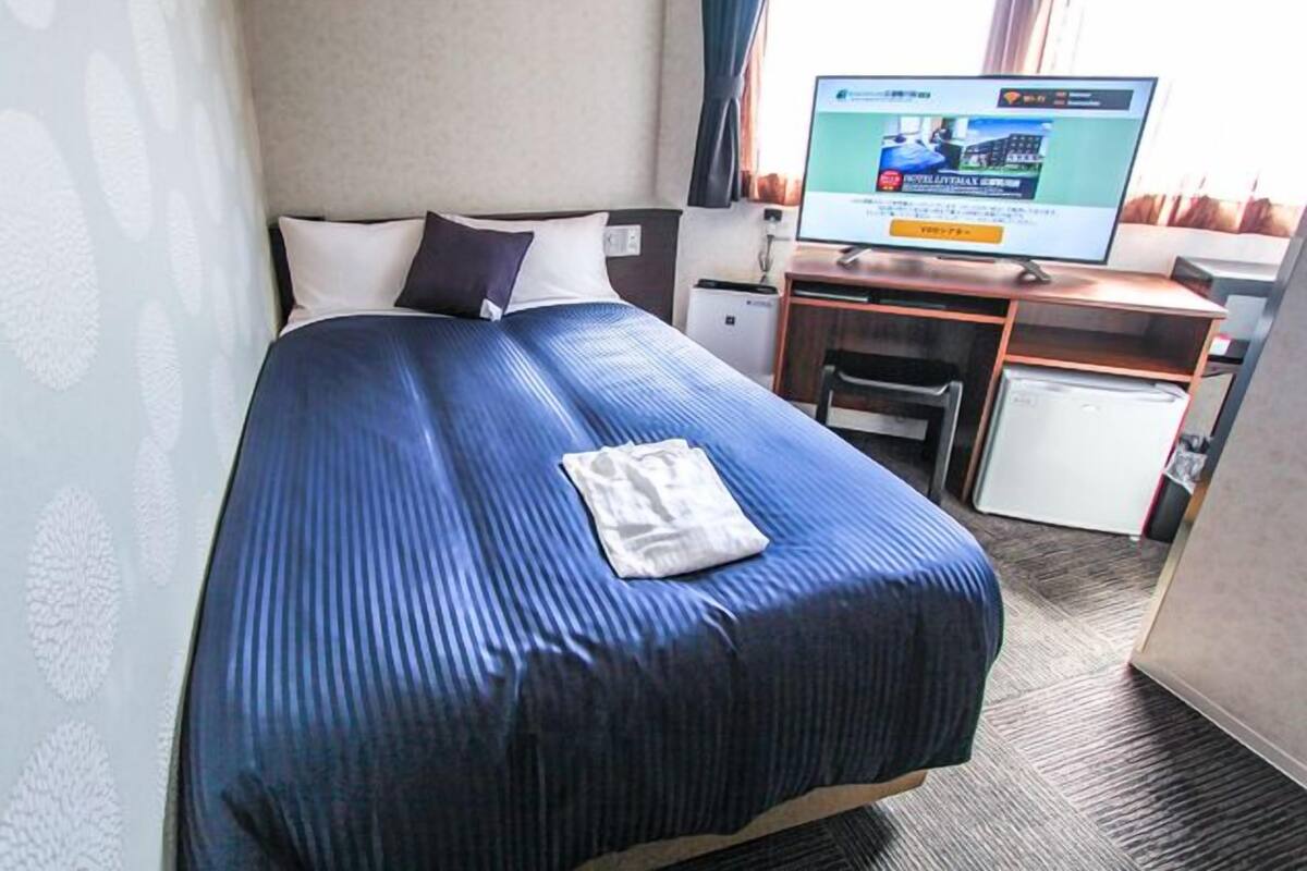 Et hotelværelse med seng, skrivebord, fjernsyn og et lille køleskab.