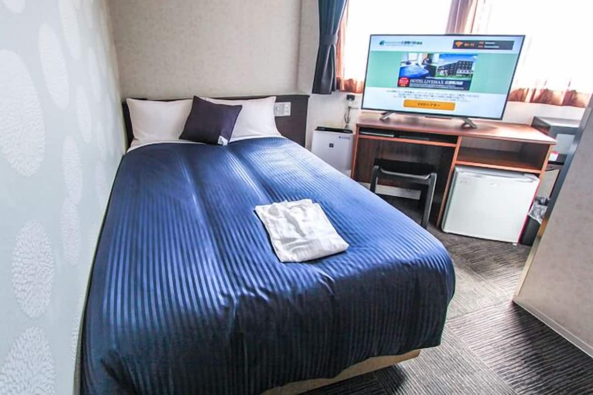 Una habitación de hotel con cama, escritorio, televisor y refrigerador pequeño.