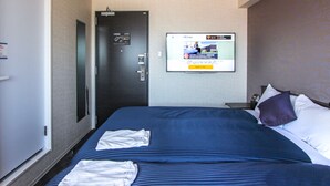 A hotel room with a bed, pillows, a nightstand, a television mounted on the wall, and a door with a lock. - HOTEL LiVEMAX Kyoto Kamogawamae (Kyoto)