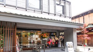 A building with a tiled entrance, a small outdoor seating area with flowers, and a signboard. - HOTEL LiVEMAX Kyoto Kamogawamae (Kyoto)