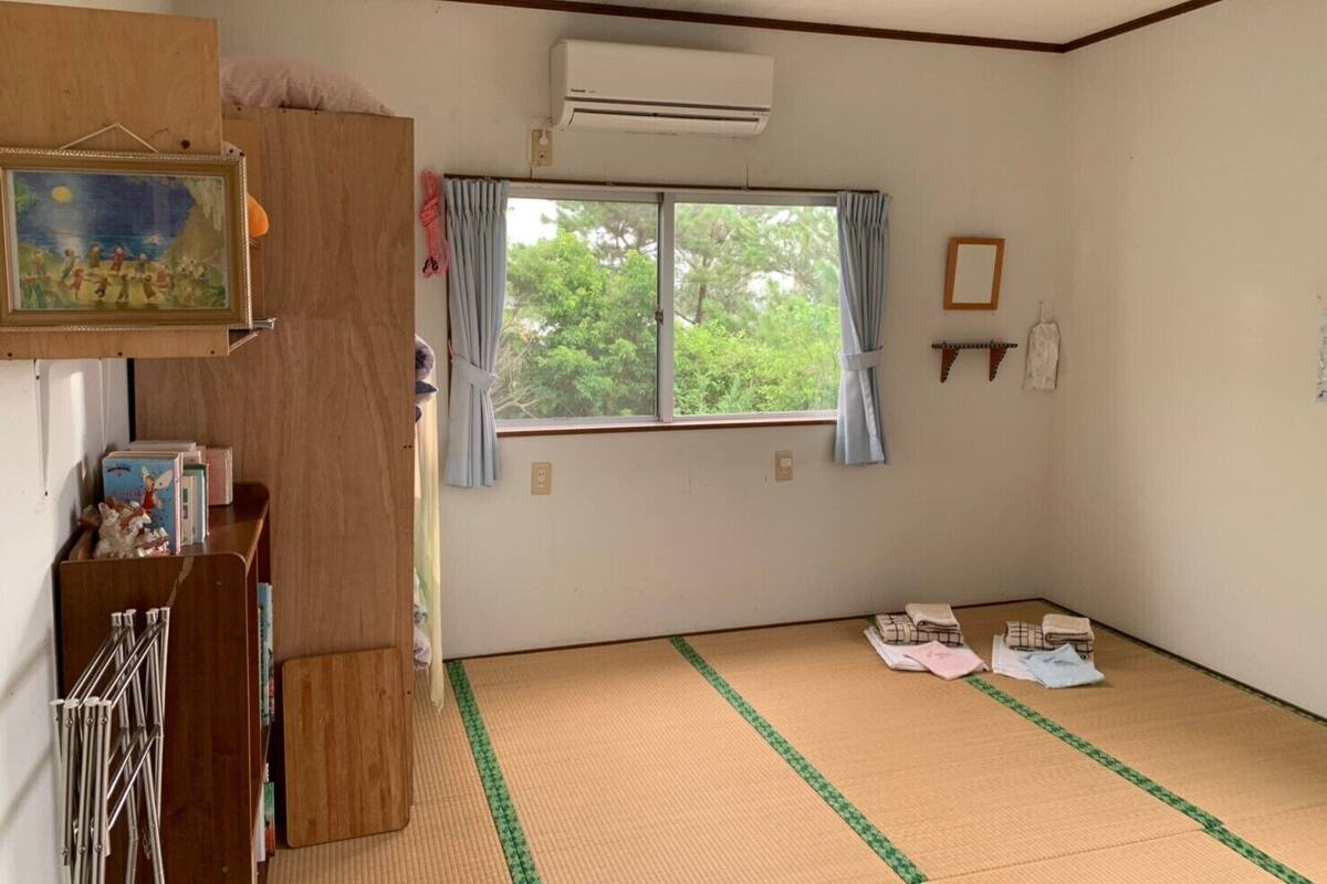 Um quarto com esteiras de tatame, uma janela com cortinas, um quadro e uma estante com livros e uma moldura.