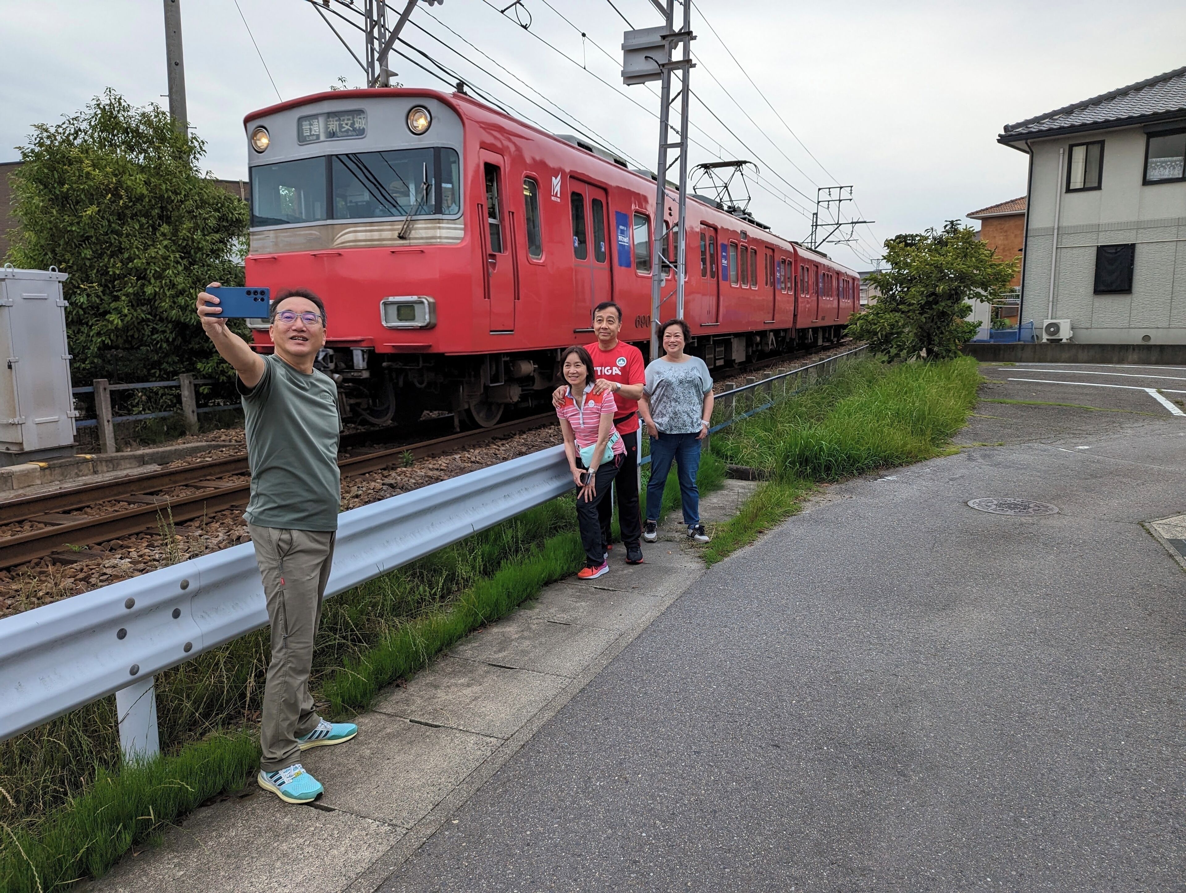 A red train on tracks with a metal guardrail and greenery beside the tracks.