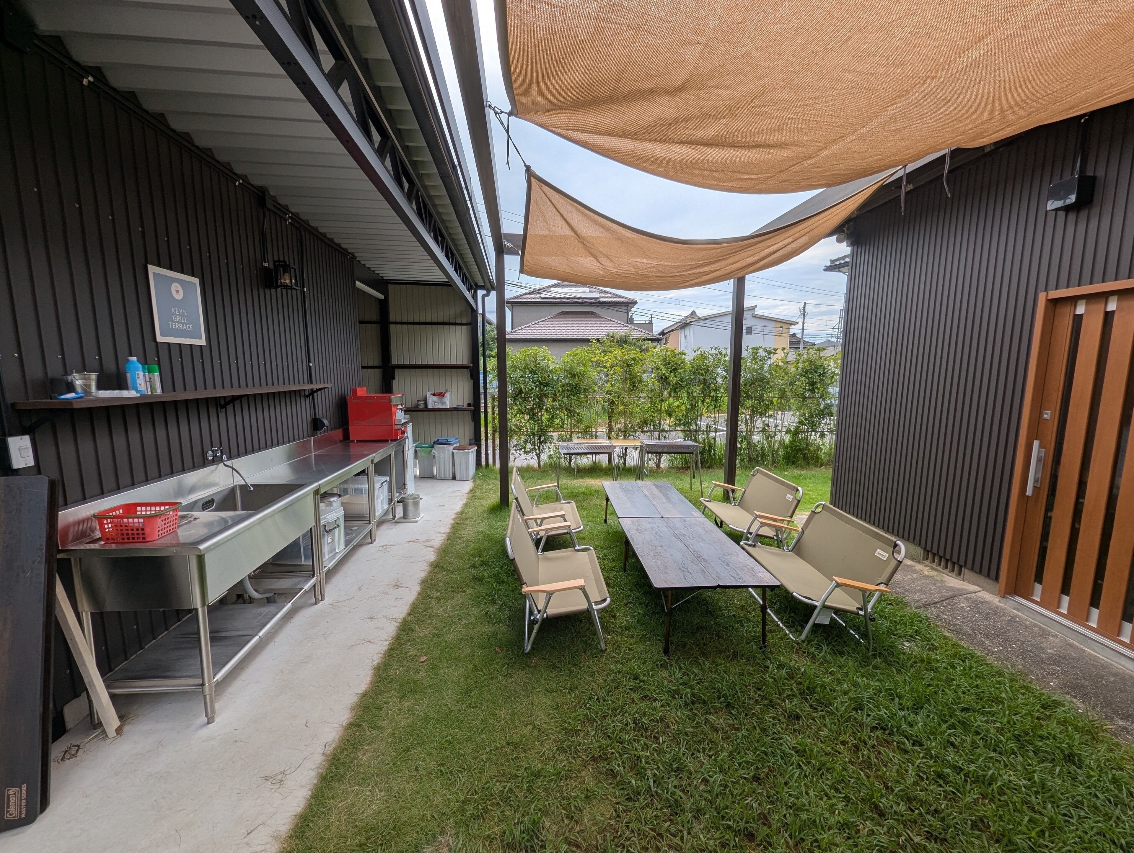 Un patio exterior con una mesa larga y sillas, una zona de barbacoa y un área sombreada con toldo.