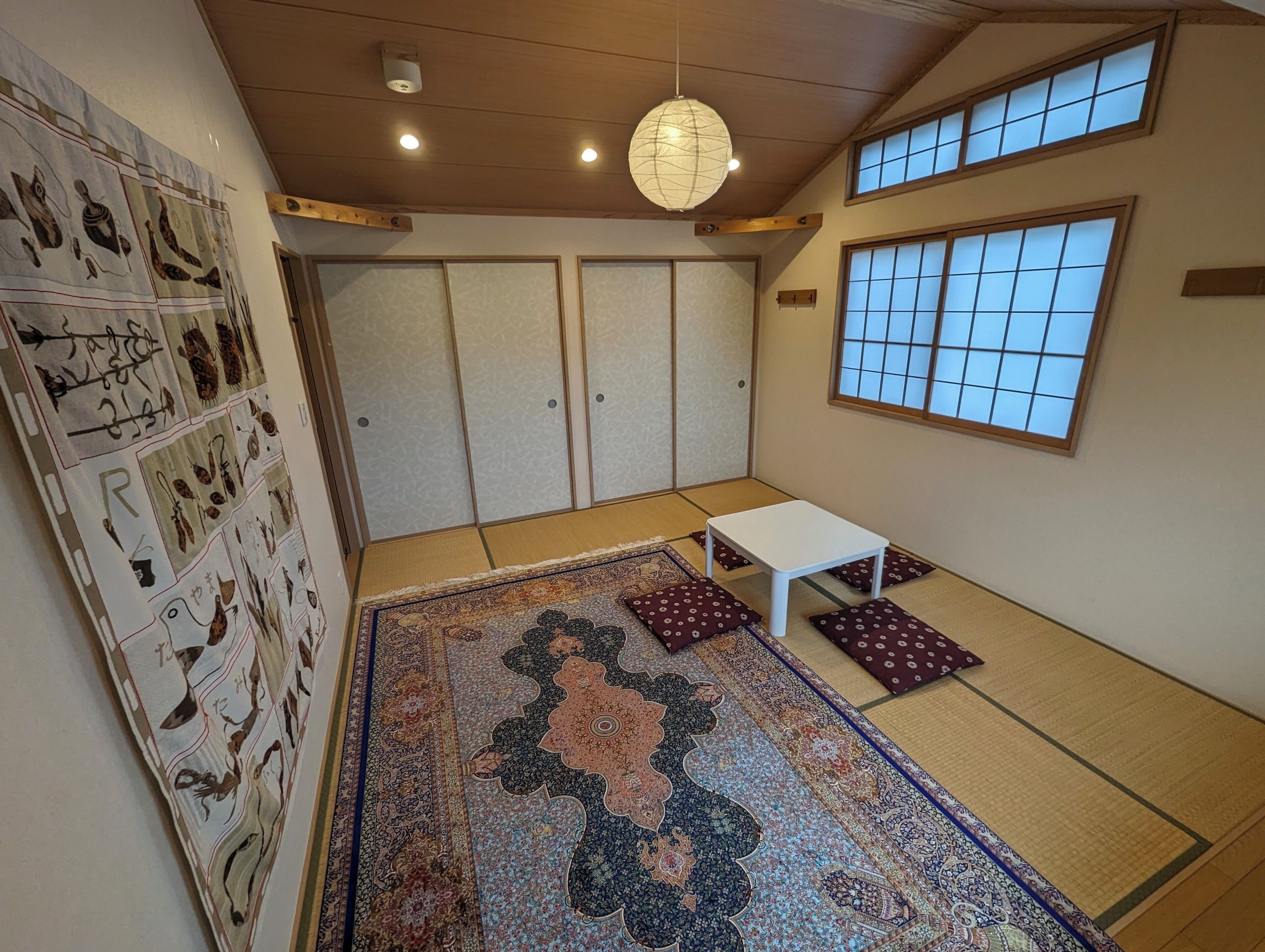 A traditional Japanese room with tatami flooring, a tatami mat with a floral pattern, a small white table, and a shoji screen door.