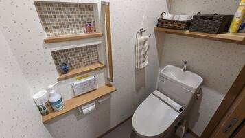 A compact bathroom with a toilet, a sink, and shelves holding toiletries and a basket.