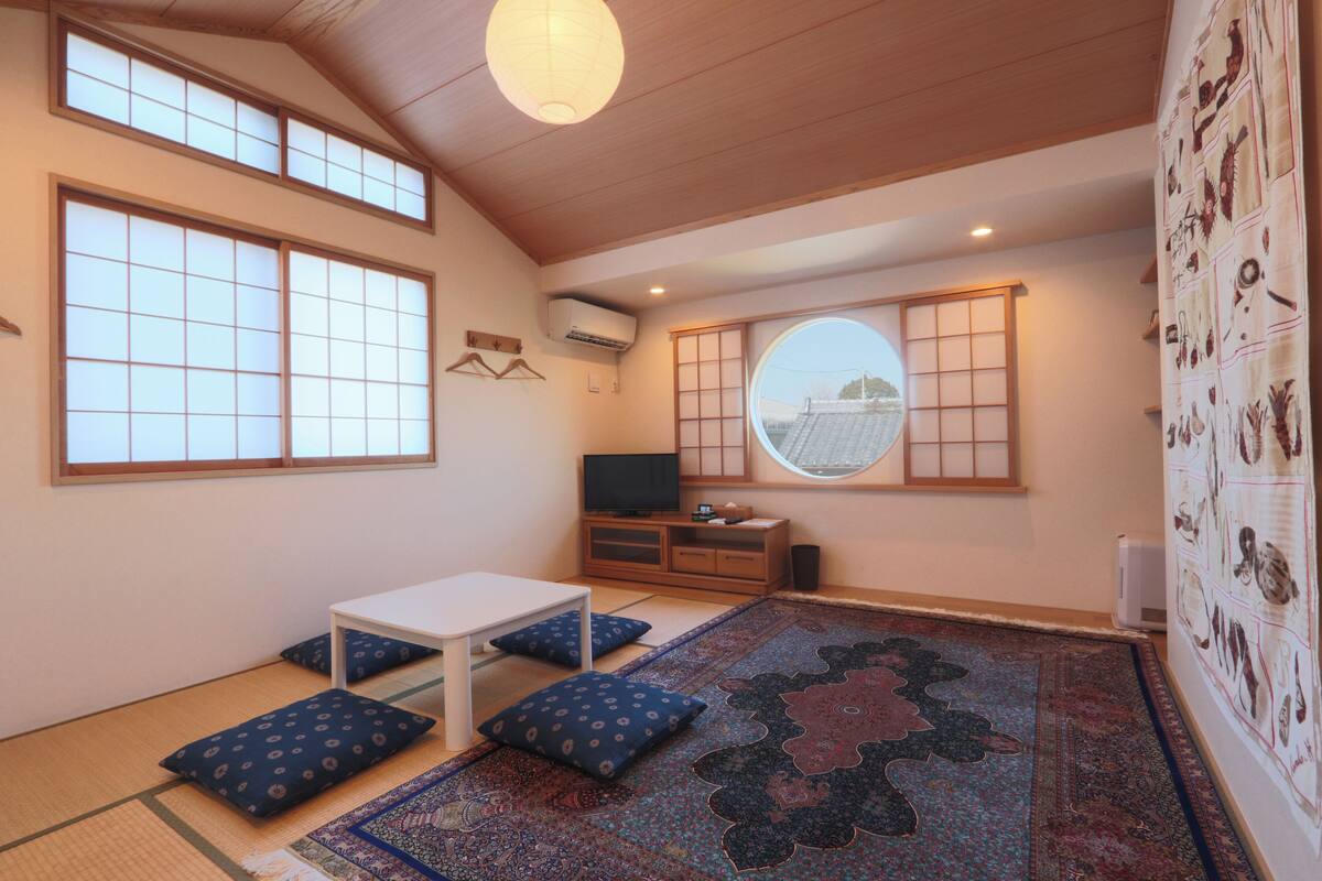 A traditional Japanese room with tatami flooring, a tatami mat table, cushions, a television, and a shoji screen.