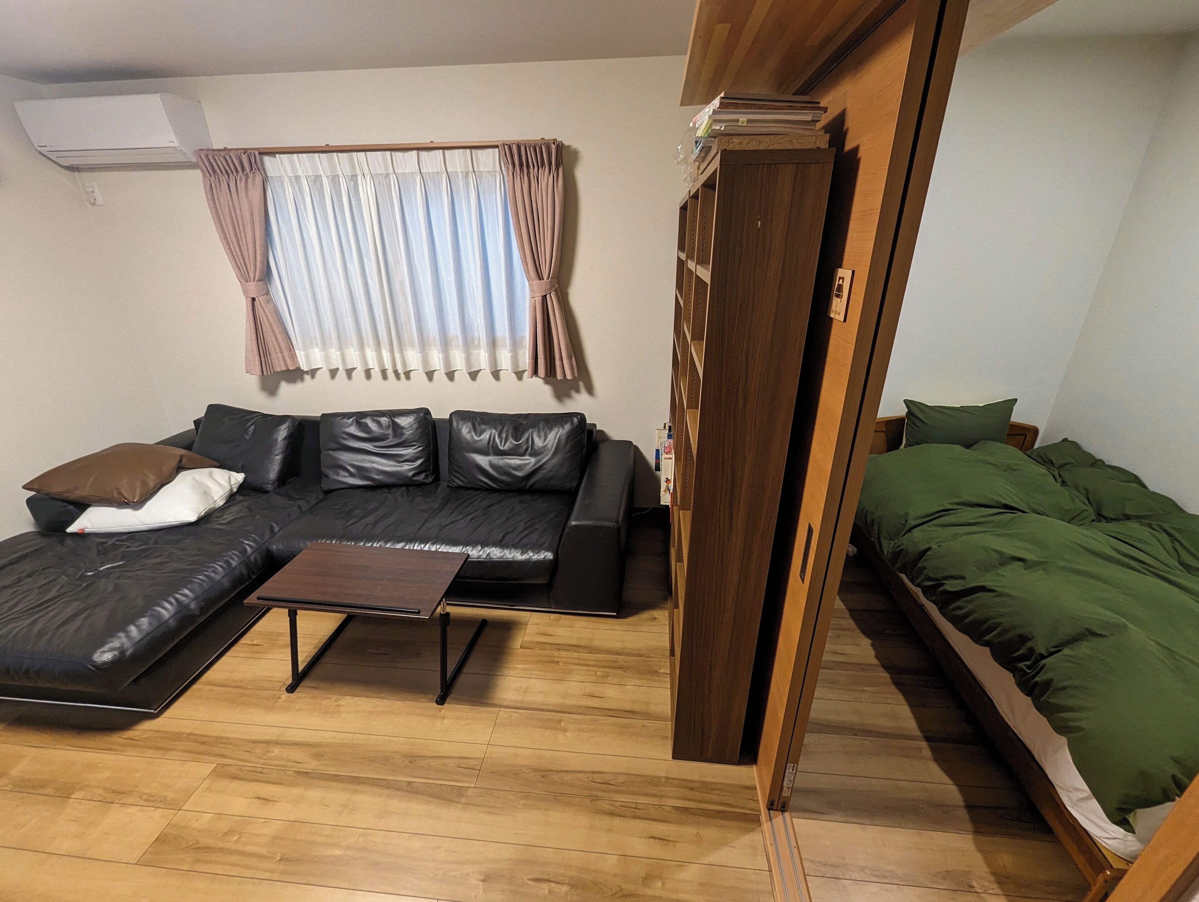A compact living space with a sofa, a small coffee table, a bed with green bedding, and a wooden wardrobe.