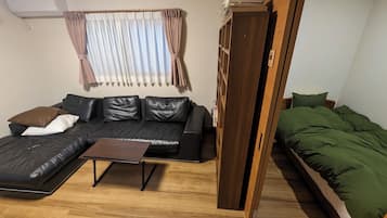 A compact living space with a sofa, a small coffee table, a bed with green bedding, and a wooden wardrobe.