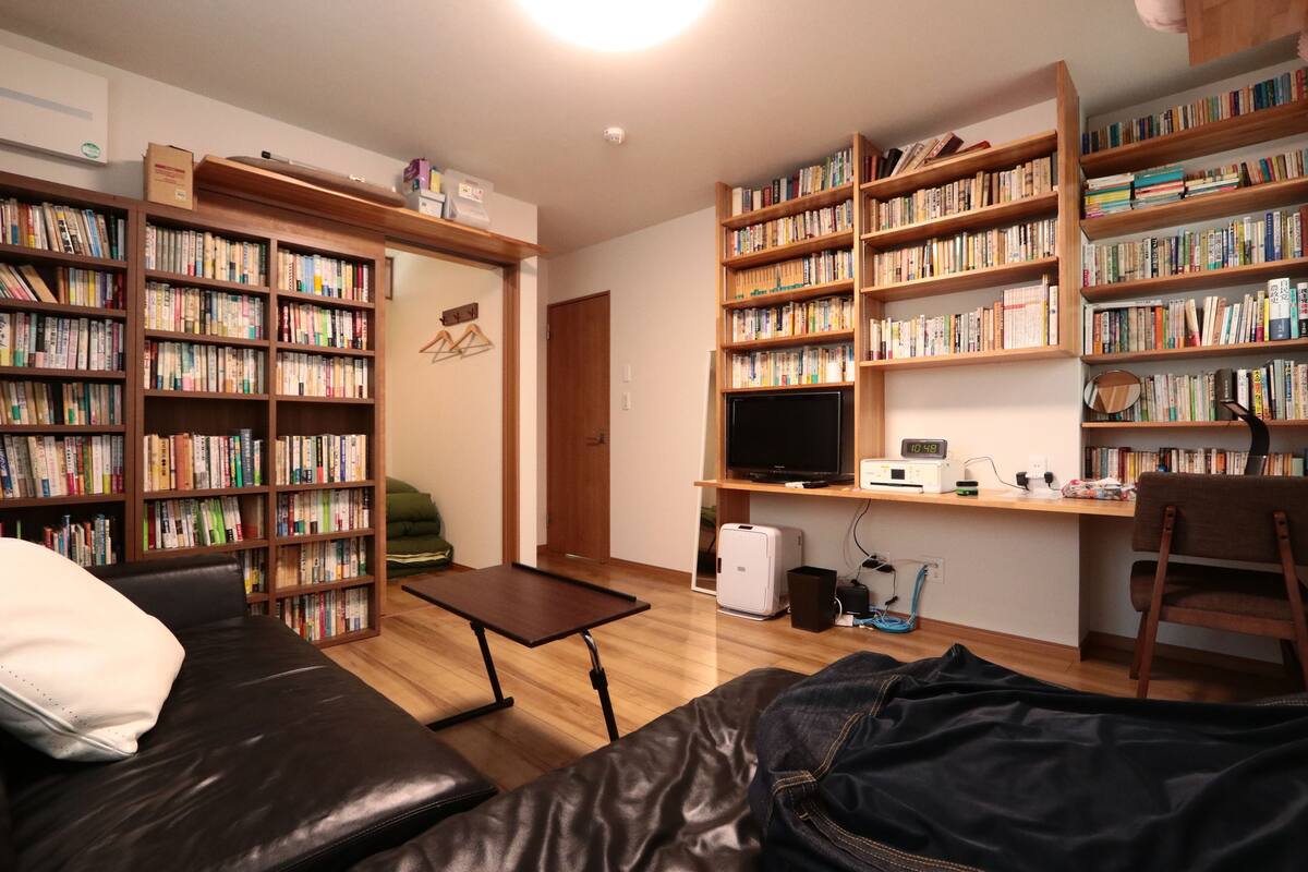 A room with a sofa, a desk with a computer, a bookshelf, and a television.