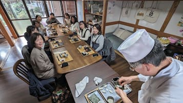 Un grup de persones assegudes al voltant d'un taula de fusta plena de safates de menjar, probablement en un restaurant o zona de menjador.