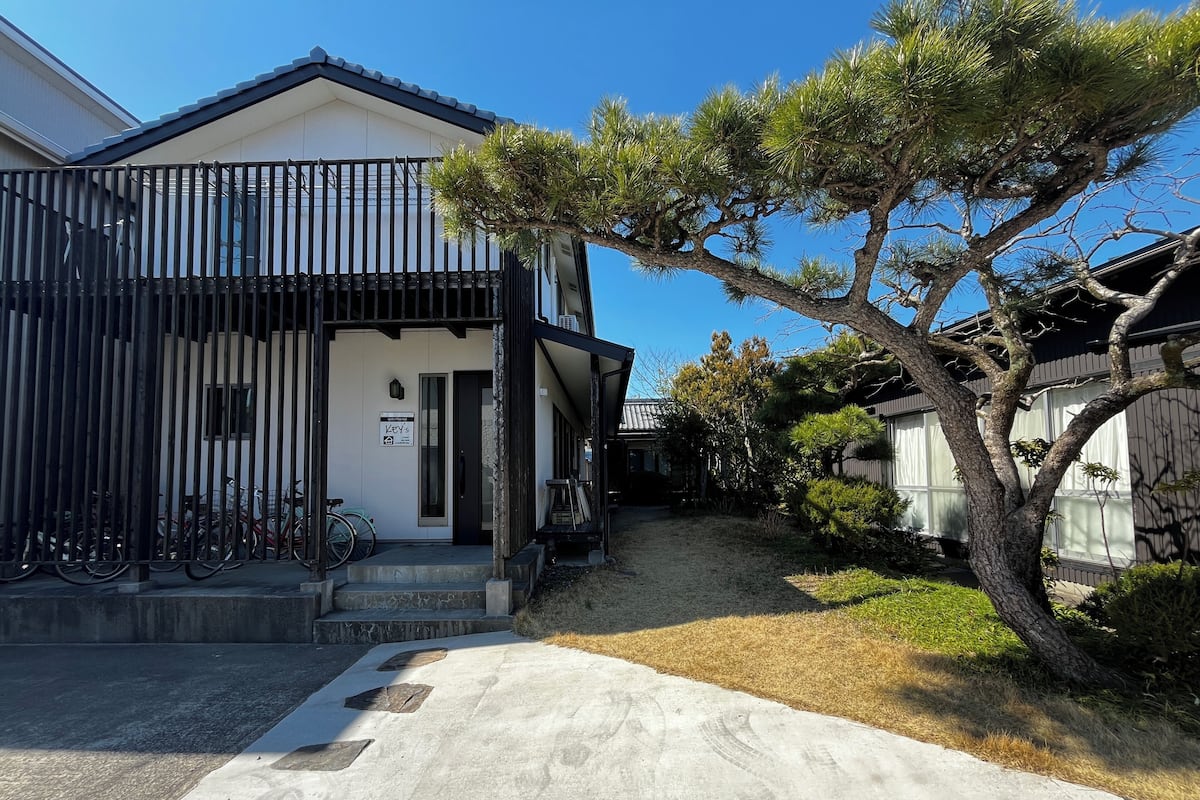 A traditional Japanese house with a black and white exterior, a stone pathway leading to the entrance, and bicycles parked outside.