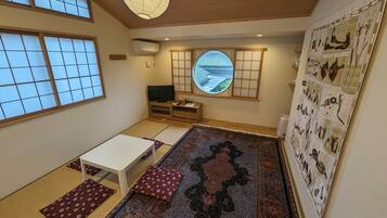 Een traditionele Japanse kamer met tatami vloeren, een lage tafel, kussens, een televisie, een shoji schuifwand en uitzicht op het omliggende landschap.