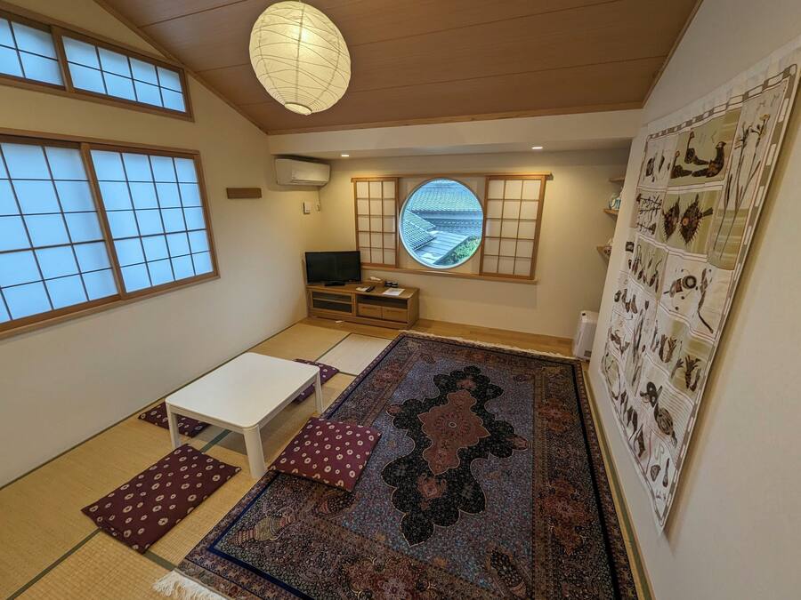 Een traditionele Japanse kamer met tatami vloeren, een lage tafel, kussens, een televisie, een shoji schuifwand en uitzicht op het omliggende landschap.