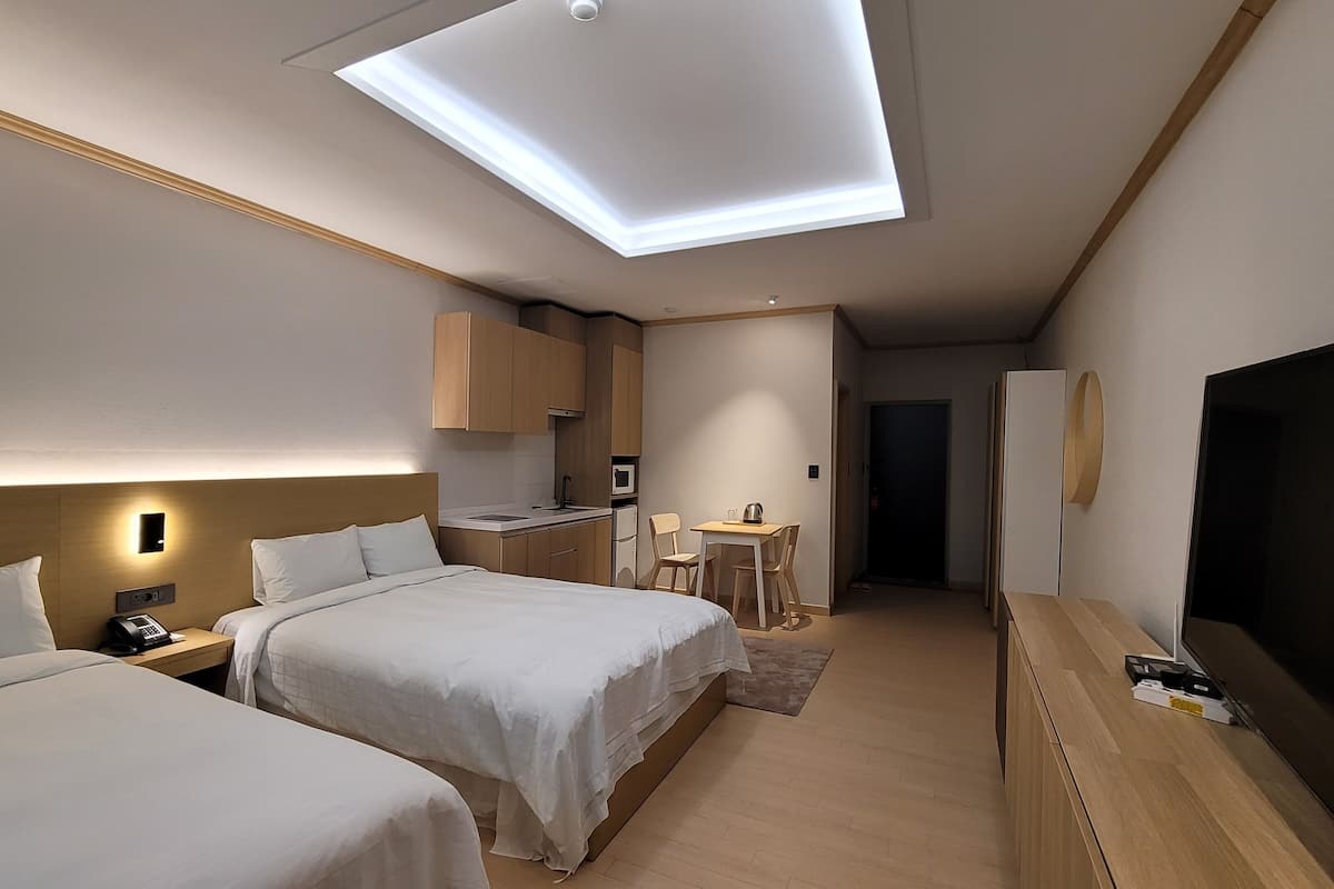 Een hotelkamer met twee bedden, een kitchenette, een televisie en een plafondlamp.