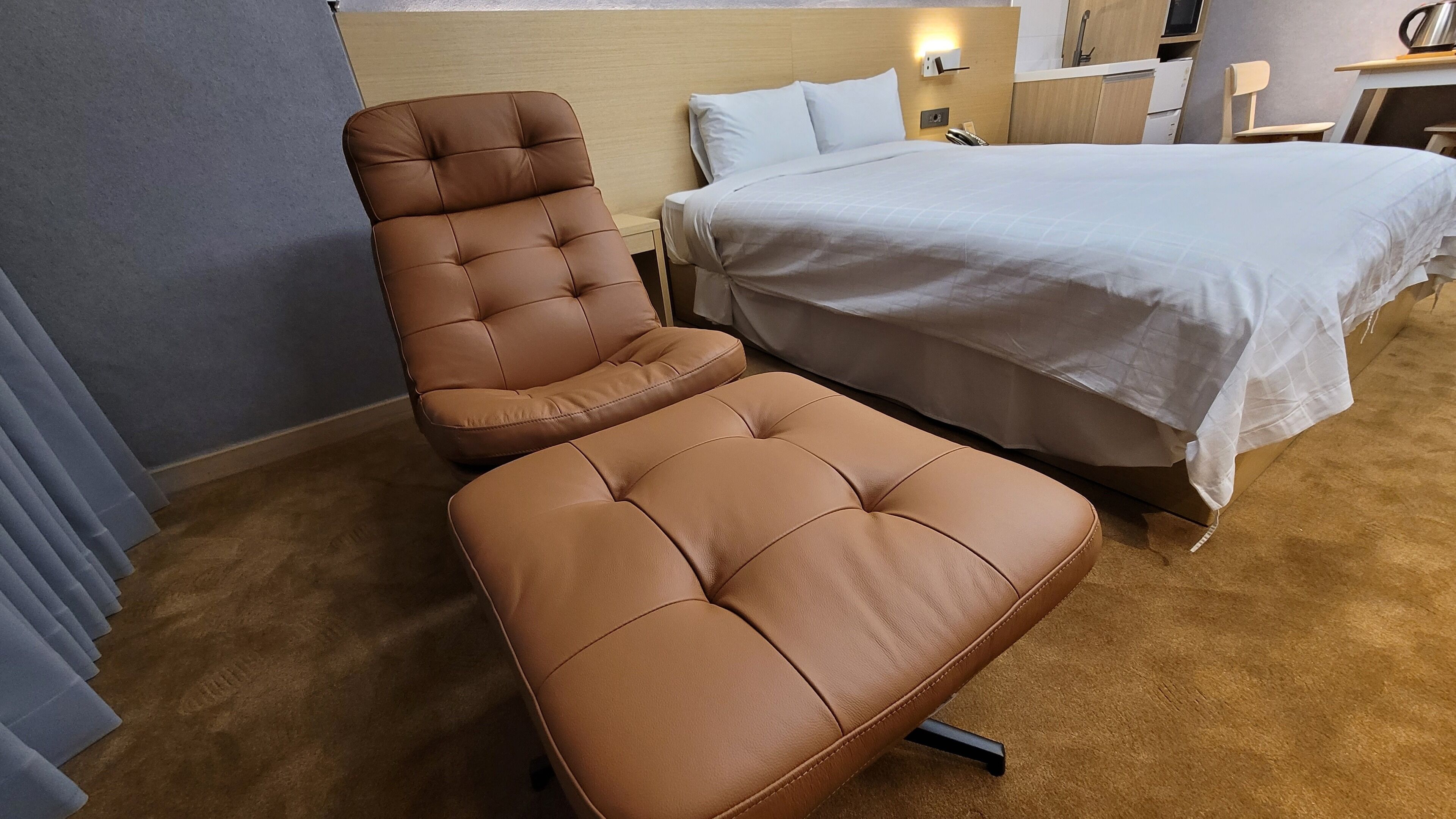 Una habitación de hotel con una cama individual, un sillón de cuero marrón y una mesita de noche pequeña.