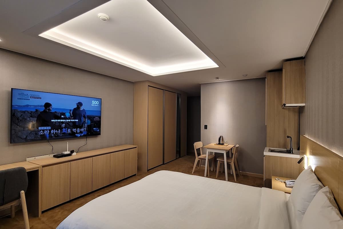 Een moderne hotelkamer met een groot bed, een bureau met stoel, een aan de muur bevestigde televisie en een kleine kitchenette.