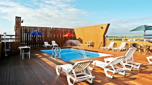 Une terrasse en bois avec une piscine, des chaises longues et des parasols.