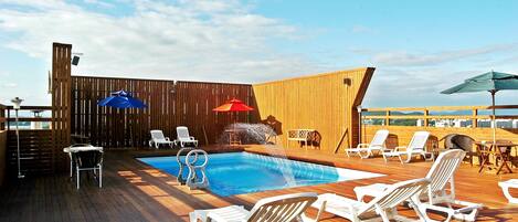 A wooden deck with a pool, lounge chairs, and umbrellas.