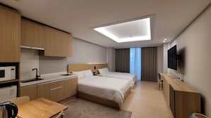 Une chambre d’hôtel équipée d’une kitchenette, de deux lits, d’un téléviseur à écran plat et d’un luminaire au plafond.