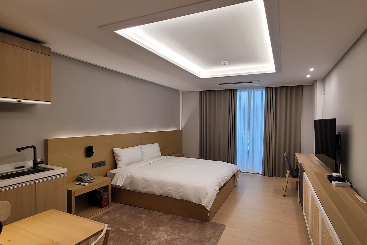 Een moderne hotelkamer met een bed, een bureau met computer, een televisie en een raam met gordijnen.