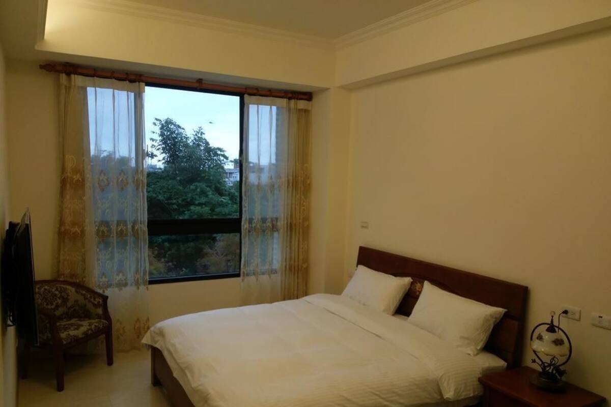A bedroom with a bed, a chair, a nightstand, and a window with curtains.