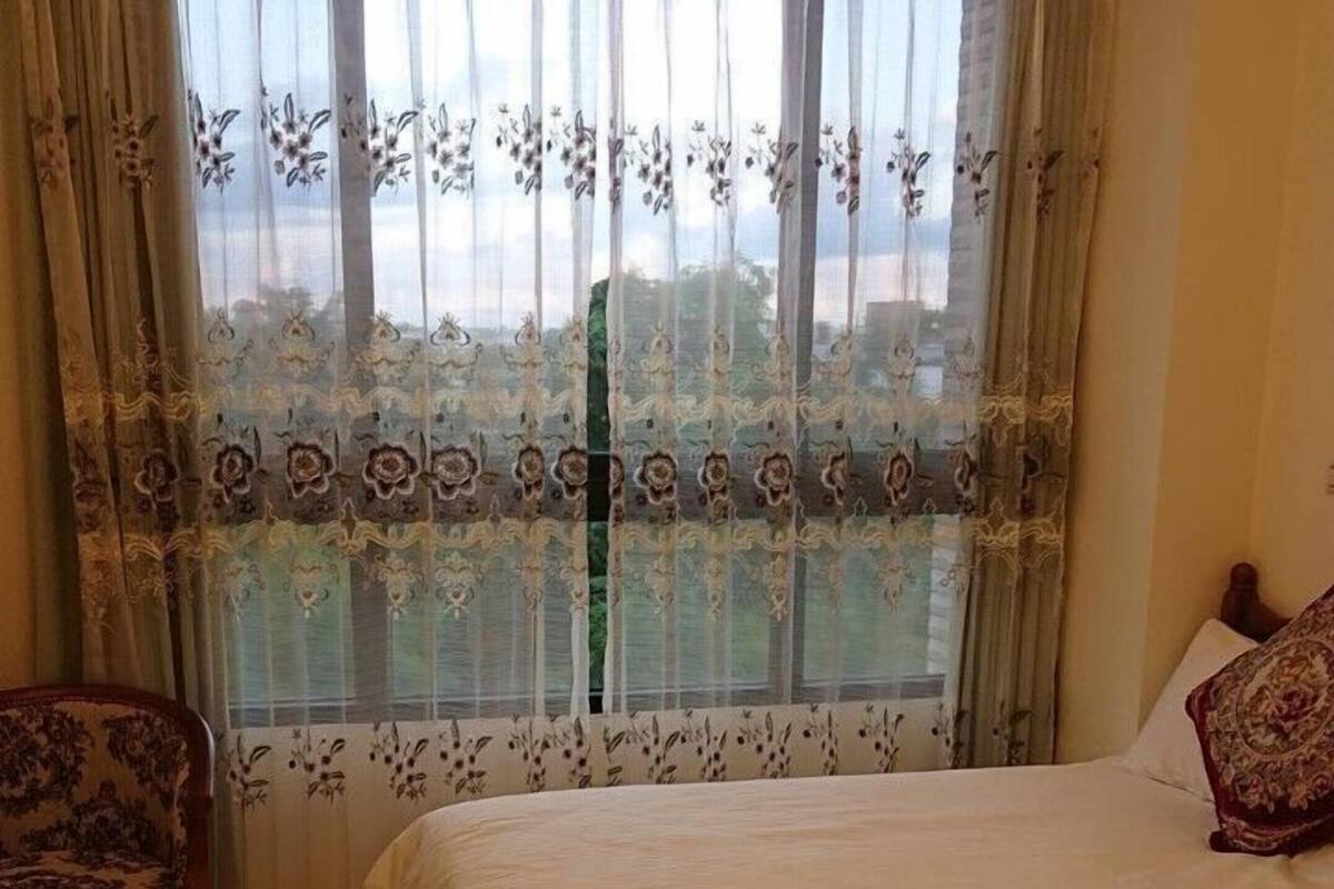 A bedroom with two beds, a chair, and a window with floral curtains.