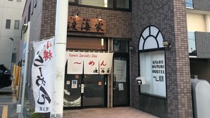 Un immeuble sur lequel on peut voir une enseigne indiquant un restaurant spécialisé dans les ramen et une auberge de jeunesse.