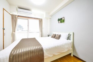 A bedroom with a bed, curtains, an air conditioning unit, and a small plant on the wall. - Yanbaru Forest Hills (Motobu)