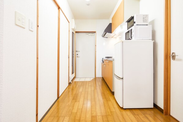 A narrow hallway with wooden flooring, a white refrigerator, a microwave, and a small kitchen area with wooden cabinets.