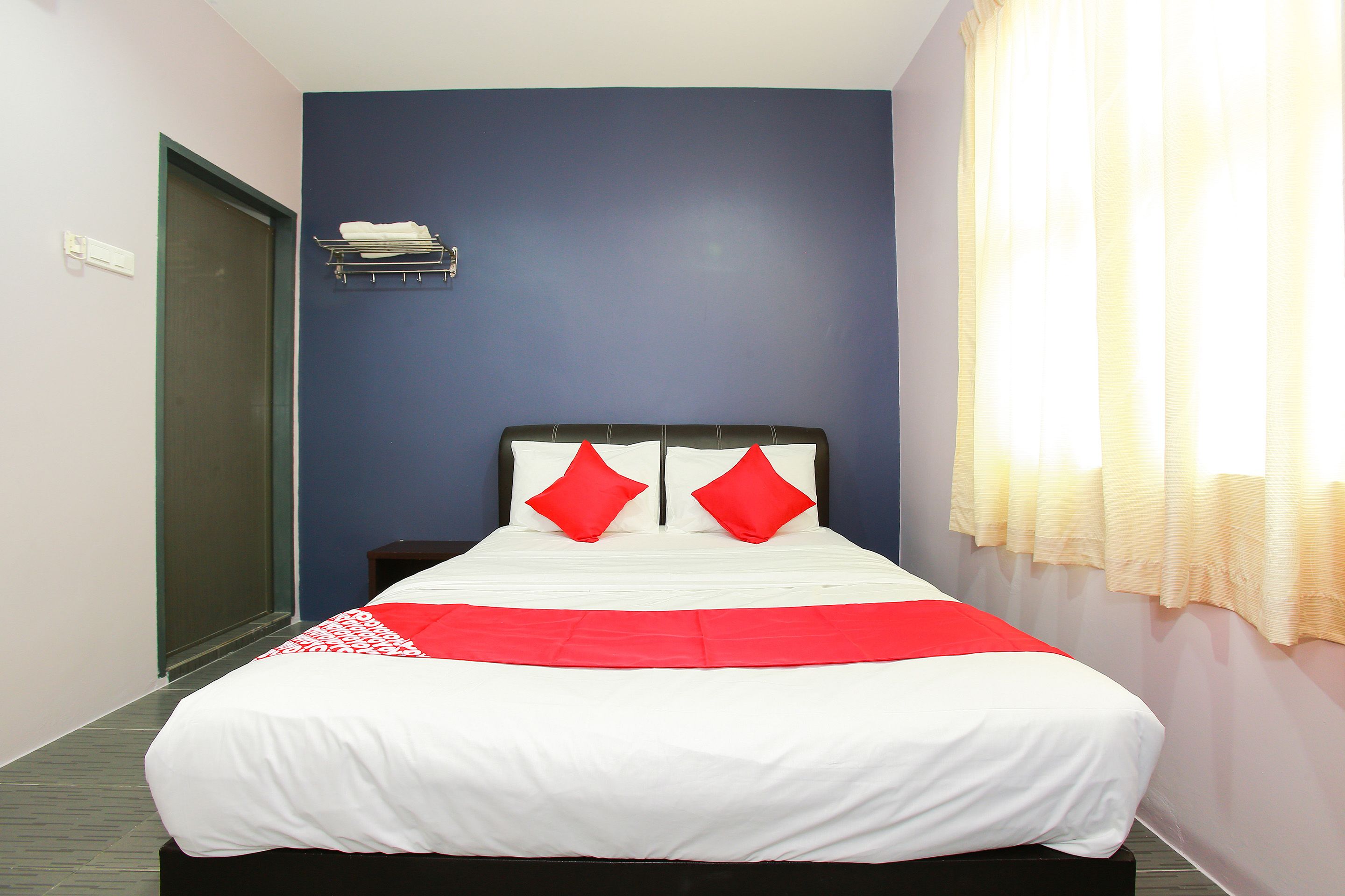 A neatly made bed with a white and red bedspread, two red pillows, and a headboard against a blue wall.