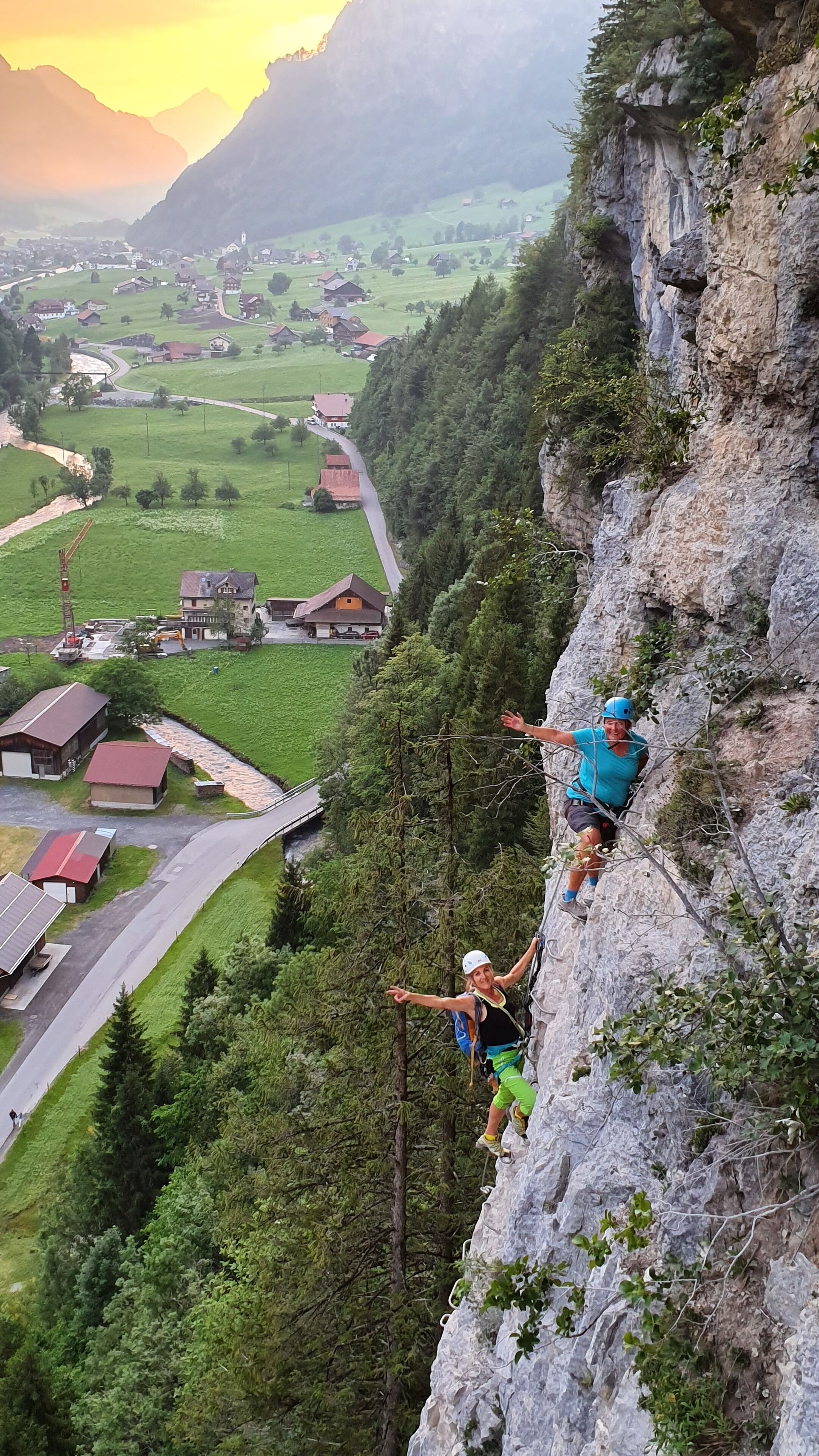 A person rappelling down a steep cliff with a village in the valley below.