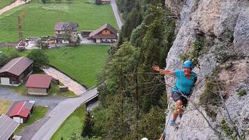 A person rappelling down a steep cliff with a village in the valley below.