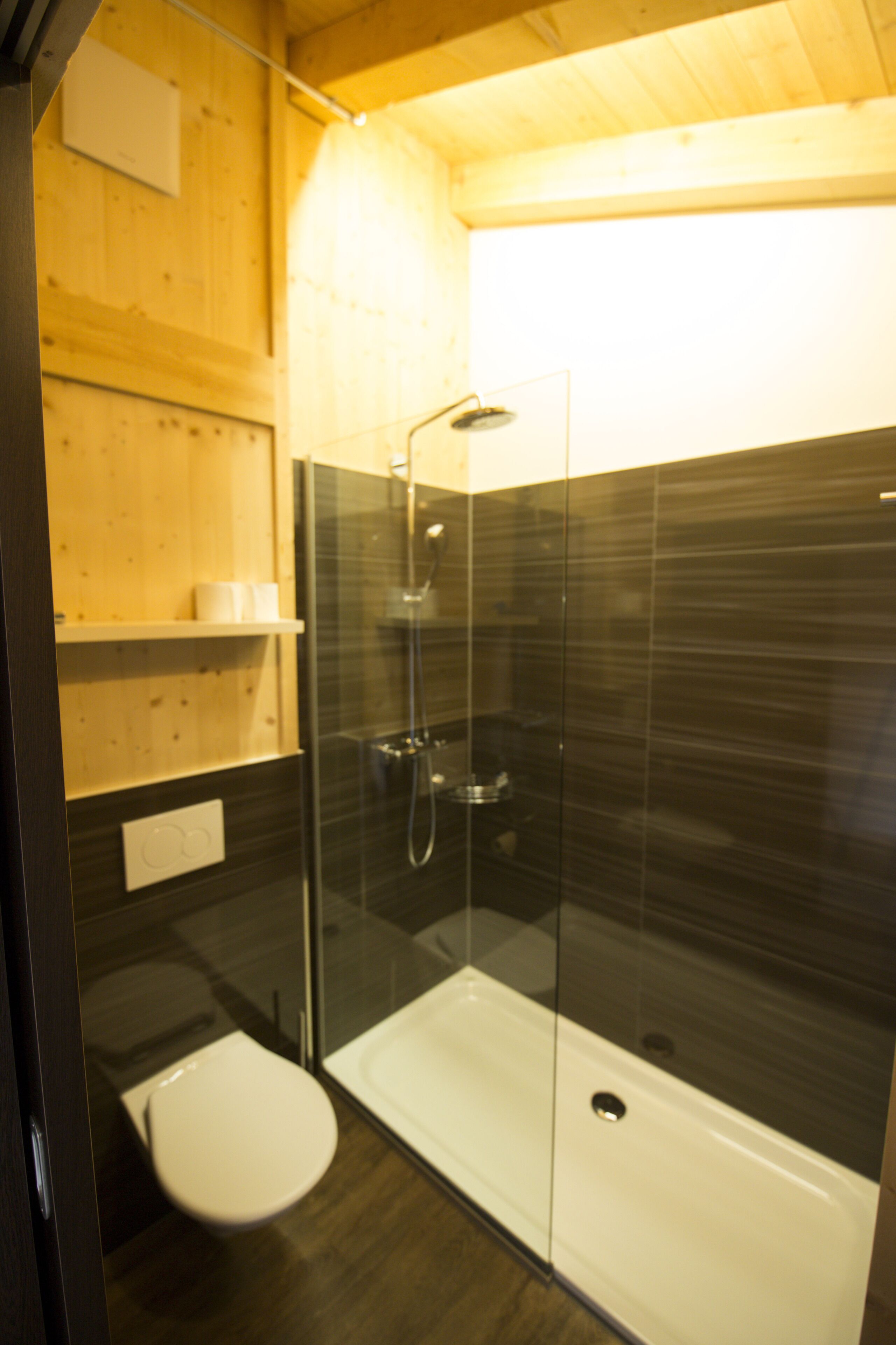 Un baño moderno con ducha envuelta en vidrio, inodoro blanco y estantes de madera.