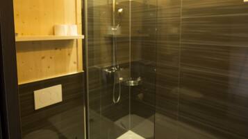Un baño moderno con ducha envuelta en vidrio, inodoro blanco y estantes de madera.